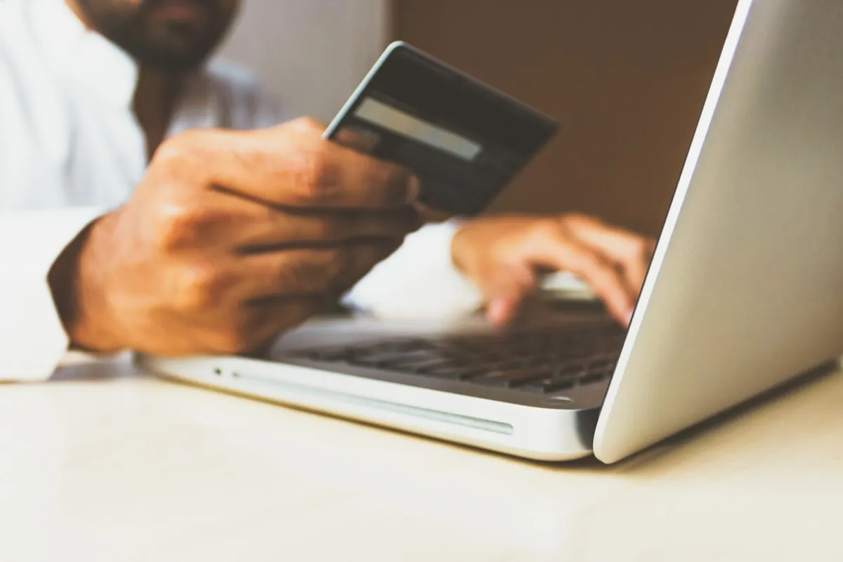 A person shopping online on a laptop, with a credit card ready for checkout.