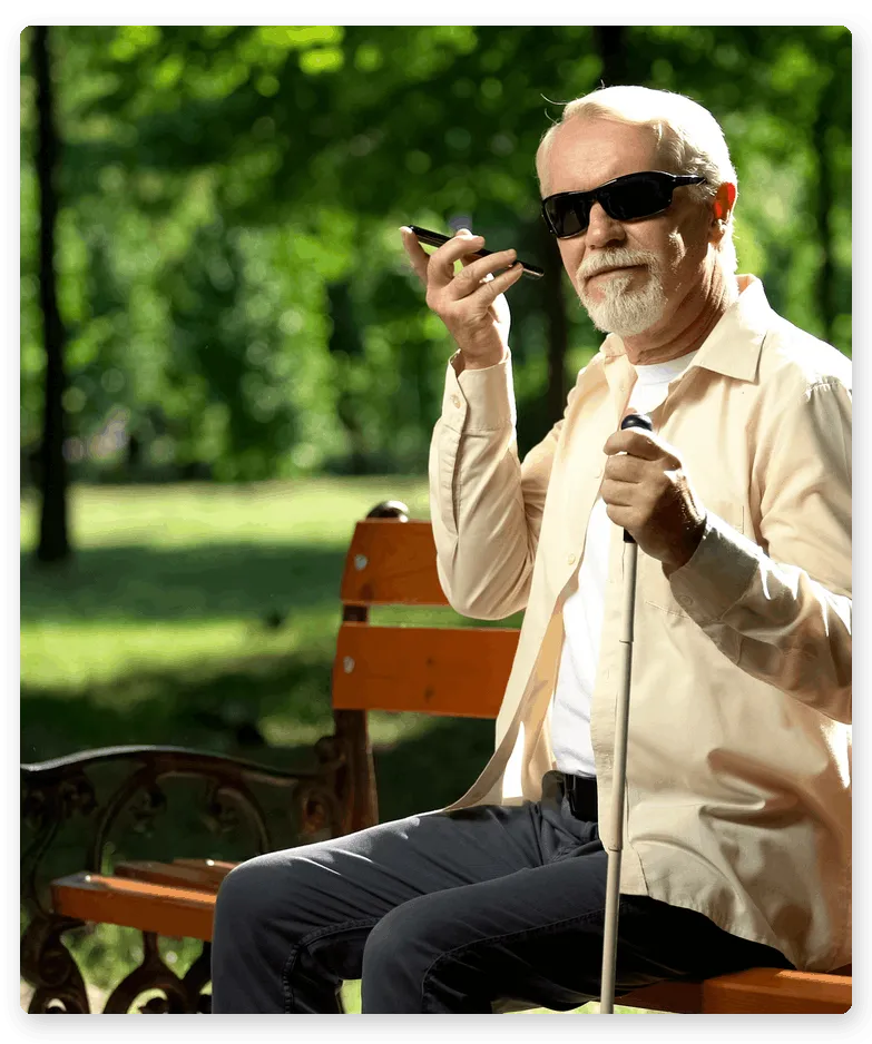 A blind man sitting on a bench listening to his mobile phone.